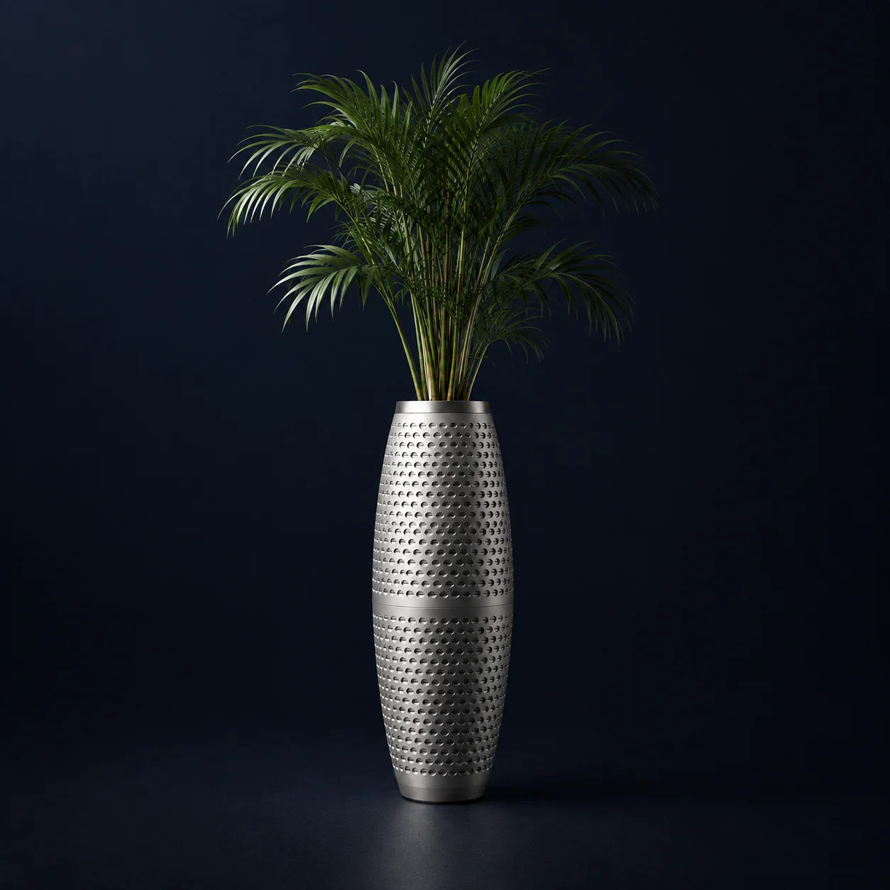 Purispira Pro, a tall brushed-steel vase with an areca palm, on a dark blue background